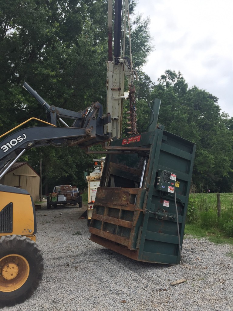 Lifting a cardboard baler with a backhoe and crane